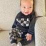 Peter is registered to the contest to win money with this photo: baby, child, smiling, sitting, couch, clothing, black_and_white, checkered_pattern, socks, hand, face, eyes, hair, indoors, portrait, comfort, furniture, cute, happy, texture