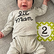 Peter is registered to the contest to win money with this photo: baby, infant, smiling, hat, clothing, pajamas, socks, couch, milestone_card, 2_months, face, happy, lying_down, indoors, textile, cozy, cute, child, person, portrait