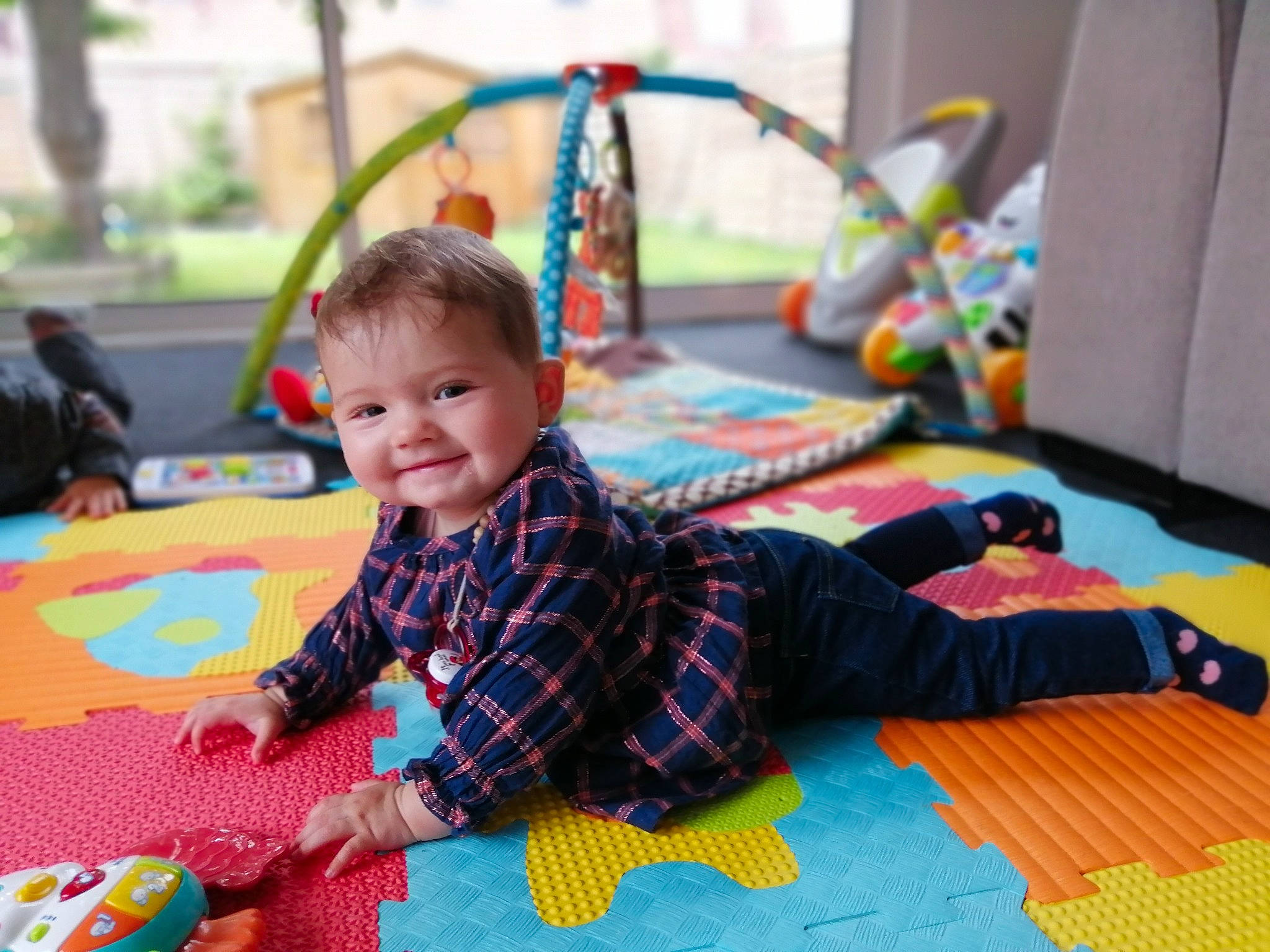 Emma a rejoint le concours — aidez-le/la à gagner de superbes lots ! baby, child, event, floor, flooring, fun, happy, joy, leisure, pattern, people, person, plaid, play, playmat, room, sitting, smile, tartan, toddler