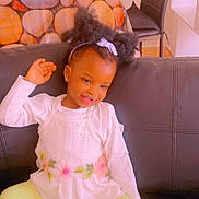 Aita Marieme participe au concours pour gagner de l'argent avec cette photo : toddler, child, sitting, couch, black_couch, white_top, yellow_pants, blue_socks, hair_ribbon, smiling, indoor, table, fruit_basket, bottle, chair, playful, cute, portrait, home, cozy
