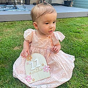 Belle is registered to the contest to win money with this photo: baby, child, cute, daylight, decor, face, girl, grass, greenery, hair_tie, happy, milestone_sign, outdoor, patio, person, pink_dress, plant, portrait, sitting, young_child