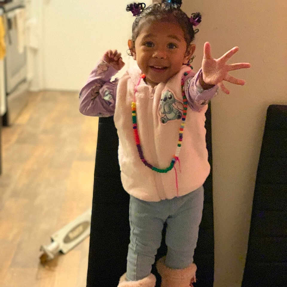 Ayrely is registered to the contest to win money with this photo: beaded_necklace, boots, cabinet, chair, child, door, floor, furniture, hair_ties, happy, home, indoor, kitchen, long_sleeve_shirt, pants, reaching, smiling, standing, toddler, vest