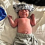 baby, infant, shirt, hat, pants, bed, blanket, bedding, clothing, lying_down, cute, child, person, skin, indoors, newborn, soft, casual, relaxed, sleepwear