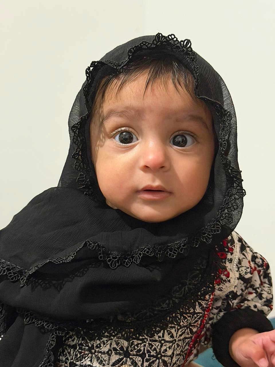 Manha joined the competition — help win amazing prizes! baby, child, face, headscarf, black_clothing, lace, patterned_clothing, wide_eyes, innocent_expression, portrait, person, young_child, cute, curious, indoors, close_up, skin, hand, head, clothing