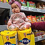 Zoe G.a joined the competition — help win amazing prizes! baby, child, girl, headband, floral_pajamas, corn_meal, grocery_store, shelf, canned_goods, snacks, yellow_box, sitting, curious, food_products, shopping_aisle, packaging, portrait, indoor, person, retail