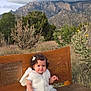 toddler, child, bench, outdoor, mountains, cloudy_sky, nature, grass, plants, desert, curly_hair, vest, barefoot, portrait, smile, young_child, wood, scenic, daytime, cute