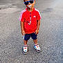 toddler, child, boy, street, sunglasses, pacifier, red_shirt, shorts, sneakers, standing, outdoor, urban, sidewalk, casual, confident, daytime, fashion, accessory, young_child, cool
