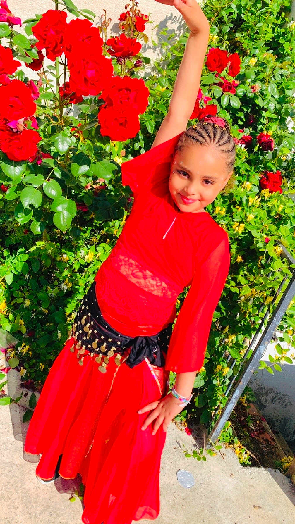 Julianna participe au concours pour gagner de l'argent avec cette photo : child, girl, red_dress, braided_hair, posing, outdoor, garden, roses, flowers, greenery, sunlight, smiling, happy, plant, nature, fashion, accessories, bracelet, concrete, wall