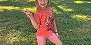 Nova is registered to the contest to win money with this photo: child, smiling, peace_sign, outdoor, grass, trees, sunlight, orange_tshirt, pink_shorts, brown_boots, nature, happy, posing, person, summer, casual_clothing, young_girl, greenery, daylight, playful