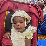 Miracle is registered to the contest to win money with this photo: baby, blurred_background, child, crowd, curious, cute, earrings, event, face, hat, indoor, infant, lemon_pattern, person, portrait, public_gathering, red_stroller, seated, stroller, yellow_clothing
