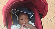 Miracle is registered to the contest to win money with this photo: baby, baby_clothes, blue_hat, child, clothing, curious, cute, foot, footwear, hand, hat, indoor, infant, person, playful, red_stroller, sitting, stroller, tile_floor, young_child