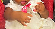 Miracle joined the competition — help win amazing prizes! baby, child, car_seat, white_dress, pacifier, red_background, cute, infant, person, portrait, indoors, young_child, holding_object, clothing, seated, looking_away, soft_lighting, adorable, toddler, closeup