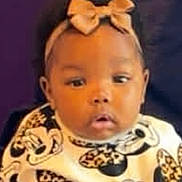 Miracle is registered to the contest to win money with this photo: baby, child, person, headband, bow, patterned_clothing, hand, adult_hand, portrait, indoor, curious, cute, infant, face, young_child, sitting, holding, purple_background, closeup, expression