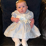 Joanie joined the competition — help win amazing prizes! baby, child, dress, white_dress, bow, socks, hair_clip, chair, leather, black_chair, indoor, portrait, cute, infant, seated, curious, young_child, fashion, baby_girl, front_view