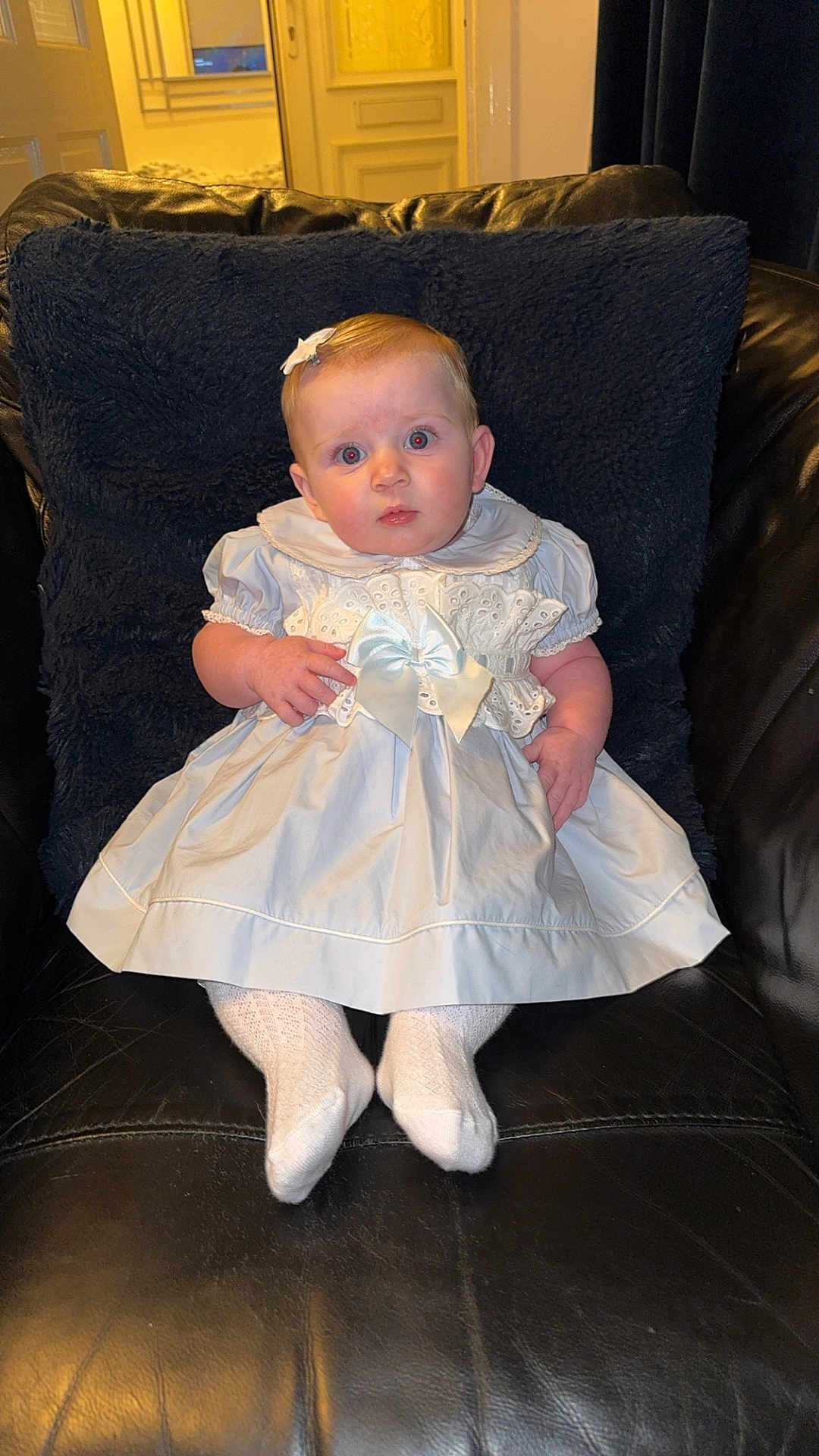Joanie joined the competition — help win amazing prizes! baby, child, dress, white_dress, bow, socks, hair_clip, chair, leather, black_chair, indoor, portrait, cute, infant, seated, curious, young_child, fashion, baby_girl, front_view