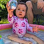 child, toddler, pool, inflatable_pool, water, toy, swimsuit, pink, fish_pattern, outdoor, grass, adult, legs, sunlight, summer, play, curious, sitting, nature, backyard