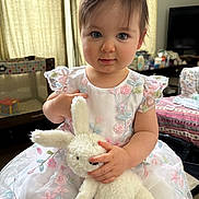Amelie joined the competition — help win amazing prizes! toddler, child, plush_toy, bunny, dress, floral_pattern, indoor, curtain, furniture, playpen, table, television, soft_toy, cute, portrait, baby, person, smile, hand, innocence