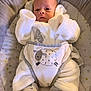 baby, infant, white_clothing, fluffy_outfit, sheep_design, baby_seat, cushion, star_pattern, footed_pajamas, newborn, cute, soft_texture, lying_down, indoors, child, face, small_hands, comfortable, warm, cozy