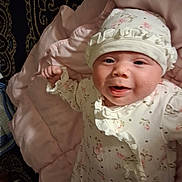 Charlotte is registered to the contest to win money with this photo: baby, infant, smile, face, hat, onesie, floral_pattern, blanket, pink, cute, child, portrait, indoors, clothing, person, soft, sleepwear, newborn, happy, laying