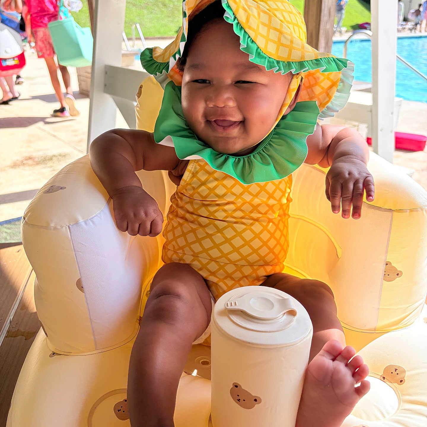 Klaryti is registered to the contest to win money with this photo: baby, infant, child, smiling, yellow_hat, pineapple_pattern, swimsuit, inflatable_chair, teddy_bear_print, poolside, outdoor, sunny, feet, happy, summer, water, people, background, hat, playful