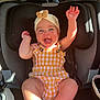baby, car_seat, child, smiling, happy, headband, yellow_clothing, checkered_pattern, arms_up, barefoot, car_interior, sunlight, seatbelt, infant, cute, joy, portrait, sitting, closeup, person