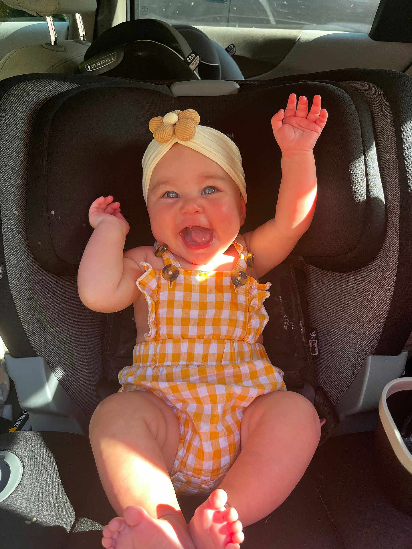 Wrenleigh joined the competition — help win amazing prizes! baby, car_seat, child, smiling, happy, headband, yellow_clothing, checkered_pattern, arms_up, barefoot, car_interior, sunlight, seatbelt, infant, cute, joy, portrait, sitting, closeup, person