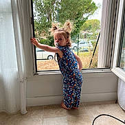 Lou a rejoint le concours — aidez-le/la à gagner de superbes lots ! barefoot, car, child, curious, curtain, daylight, fence, home, indoor, jumpsuit, looking_back, open_window, pacifier, person, pigtails, standing, tile_floor, toddler, tree, window