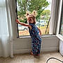 barefoot, car, child, curious, curtain, daylight, fence, home, indoor, jumpsuit, looking_back, open_window, pacifier, person, pigtails, standing, tile_floor, toddler, tree, window