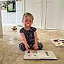 Lou a rejoint le concours — aidez-le/la à gagner de superbes lots ! blue_clothing, book, child, curious, door, floor, home, indoor, kitchen, oven, pacifier, patterned_clothing, person, reading, refrigerator, sitting, tiles, toddler, toy, young_child