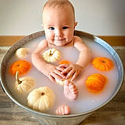 Asher joined the competition — help win amazing prizes! autumn_theme, baby, bath, cute, face, feet, hands, infant, metal_tub, milk_bath, milky_water, neutral_wall, orange_pumpkin, portrait, props, pumpkin, sitting, smiling, white_pumpkin, wooden_floor