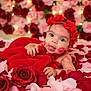 baby, flower_crown, red_blanket, rose_petals, lipstick_kiss, tongue_out, cute, infant, playful, portrait, close_up, decorative_lights, soft_texture, pink_roses, red_roses, skin, face, hand, lying_down, adorable