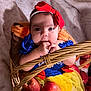 baby, infant, child, basket, apples, red_bow, blue_dress, yellow_skirt, hand, face, headband, fruit, cute, indoors, soft_blanket, plush, portrait, closeup, person, costume