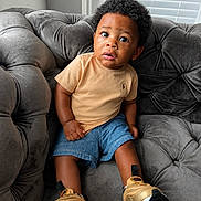 Leonidas joined the competition — help win amazing prizes! child, toddler, baby, portrait, sitting, sofa, couch, curly_hair, smiling, wide_eyes, indoor, living_room, window, blinds, gray_furniture, tan_shirt, denim_shorts, golden_shoes, fashion, photography