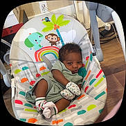 Nehemiah Jr is registered to the contest to win money with this photo: baby, infant, baby_seat, mittens, socks, pacifier, wooden_floor, colorful, animal_illustration, monkey, elephant, rainbow, palm_tree, indoors, child, cute, relaxed, clothing, floor, seat