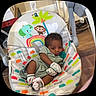 baby, infant, baby_seat, mittens, socks, pacifier, wooden_floor, colorful, animal_illustration, monkey, elephant, rainbow, palm_tree, indoors, child, cute, relaxed, clothing, floor, seat