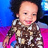afro_hair, baby, bear_pattern, bed, bottle, bright_colors, child, clothing, cute, earrings, happy, indoors, pajamas, person, pink_bedspread, portrait, seated, smiling, toddler, young_child