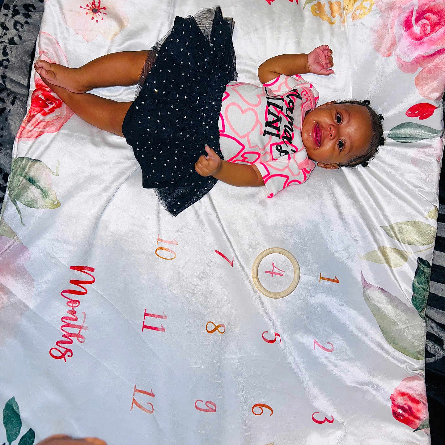 Emonnie is registered to the contest to win money with this photo: baby, blanket, child, clothing, cute, face, floral_pattern, hand, happy, head, indoor, infant, lying_down, months_marker, person, portrait, shirt, skin, skirt, smiling
