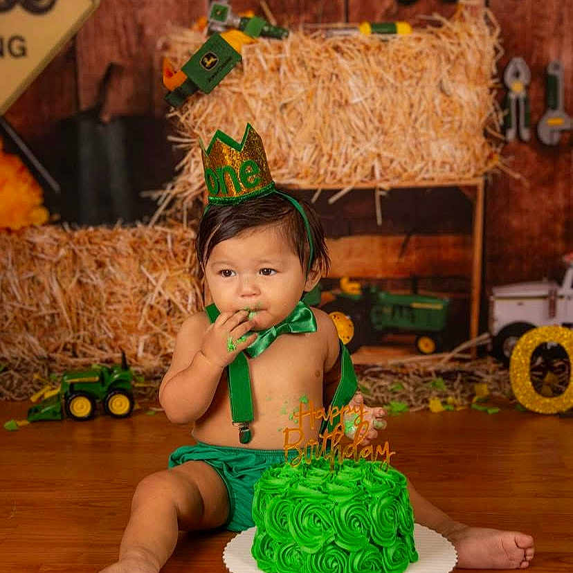Zealand joined the competition — help win amazing prizes! baby, birthday, birthday_cake, cake, child, costume, farmer_theme, festive, food, green, hay_bales, indoor, portrait, sitting, smiling, toy_tractors, toddler, wooden_floor, party_hat, celebration