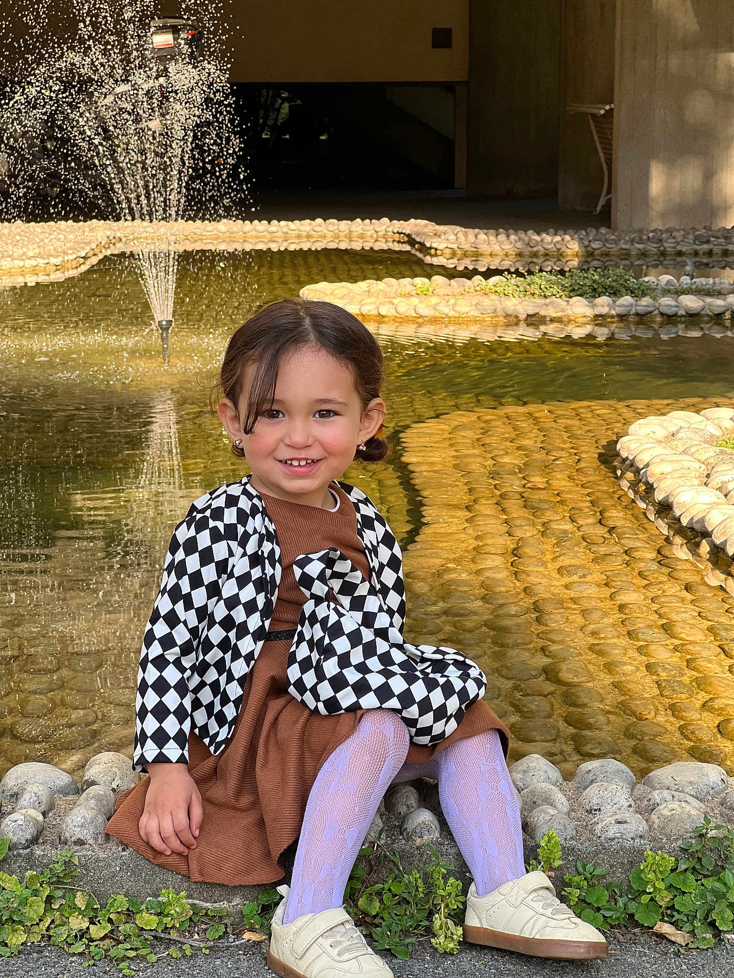 Rita a rejoint le concours — aidez-le/la à gagner de superbes lots ! casual, child, dress, fashion, fountain, girl, greenery, happy, jacket, outdoor, plants, pond, shoes, sitting, smiling, stone, sunlight, tights, water, young