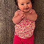Myla is registered to the contest to win money with this photo: baby, child, smiling, happy, clapping, ponytail, floral_top, pink_shorts, barefoot, lying_down, rug, textured_rug, cute, portrait, infant, indoors, young_child, skin, person, toddler