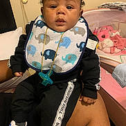 Jyzere is registered to the contest to win money with this photo: baby, infant, bib, pacifier, tracksuit, black_clothing, elephant_pattern, sneakers, adults_lap, plush_toys, nursery, indoor, child, cute, person, footwear, toy, seated, portrait, home