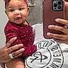baby, child, person, adult, mirror, selfie, phone, headband, bow, polka_dot, maroon, clothing, hand, ring, smile, dimples, face, bathroom, tiles, casual