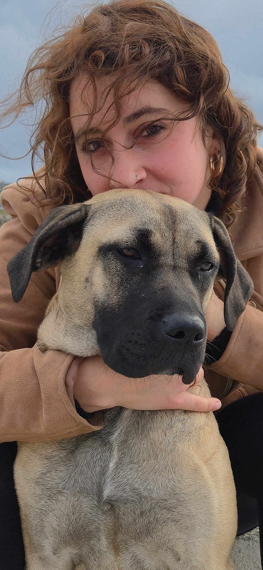 Kraze a rejoint le concours — aidez-le/la à gagner de superbes lots ! affection, animal, brown_coat, calm, candid, casual_clothing, close_up, curly_hair, dog, earrings, embrace, face, friendship, large_dog, nose_ring, outdoor, overcast_sky, person, pet, portrait