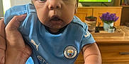 Suliman joined the competition — help win amazing prizes! baby, child, indoor, football_kit, manchester_city, sportswear, television, soccer, hand, curly_hair, person, carpet, furniture, plant, flower_pot, living_room, sports, cute, wide_eyes, curious