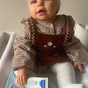 Lya participe au concours pour gagner de l'argent avec cette photo : baby, child, infant, headband, bow, clothing, checkered, sitting, changing_pad, cream, tube, hand, white_tights, portrait, indoors, soft_lighting, face, cute, baby_care, neutral_background