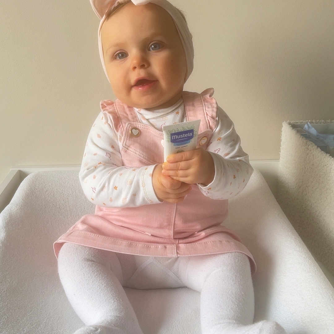 Lya participe au concours pour gagner de l'argent avec cette photo : baby, bow, child, clothing, cozy, cream_tube, cute, framed_print, happy, headband, indoors, mustela, neutral_wall, person, pink_dress, portrait, sitting, soft_lighting, white_tights, young_child