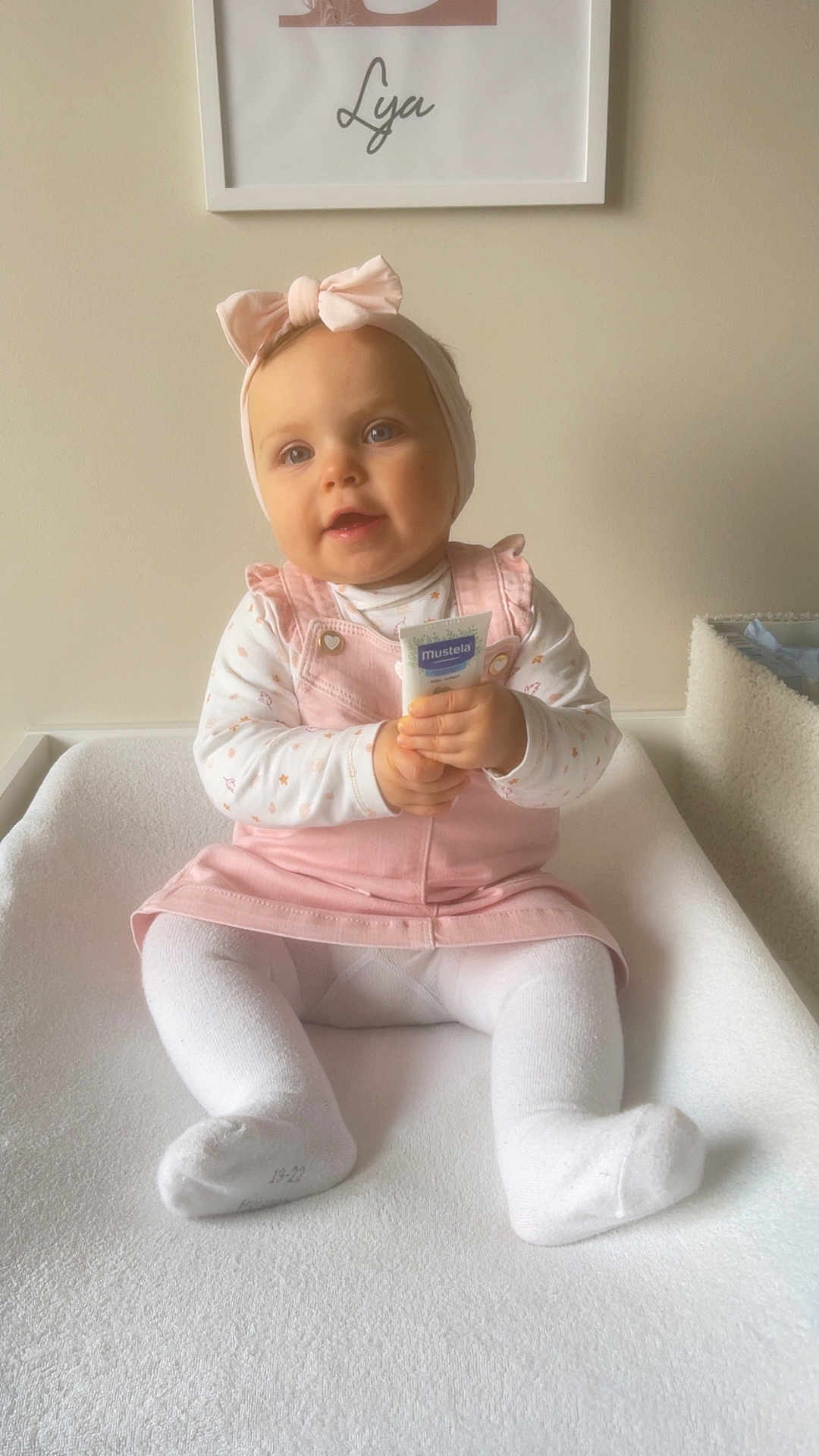 Lya participe au concours pour gagner de l'argent avec cette photo : baby, child, pink_dress, headband, bow, white_tights, sitting, cream_tube, mustela, indoors, cozy, soft_lighting, neutral_wall, framed_print, cute, portrait, young_child, happy, clothing, person