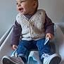 toddler, child, smiling, sitting, shoes, jeans, vest, long_sleeve, indoor, changing_table, happy, person, footwear, casual_clothing, baby, holding, white, blue, cozy, cute