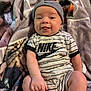 Reed is registered to the contest to win money with this photo: baby, infant, smiling, beanie, onesie, nike_logo, blanket, cozy, lying_down, chubby_legs, hands, toes, cute, portrait, indoor, soft_texture, patterned_blanket, close_up, happy, playful