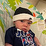 Reed is registered to the contest to win money with this photo: baby, infant, face, eyes, beanie, hat, nike_logo, onesie, clothing, bouncer_seat, patterned_fabric, leaf_pattern, indoor, portrait, cute, hands, skin, close_up, seat_label, expression